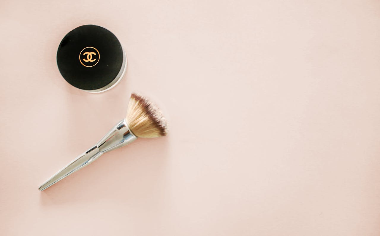 Sophisticated flatlay of a makeup brush and branded cosmetic jar on a pastel background.